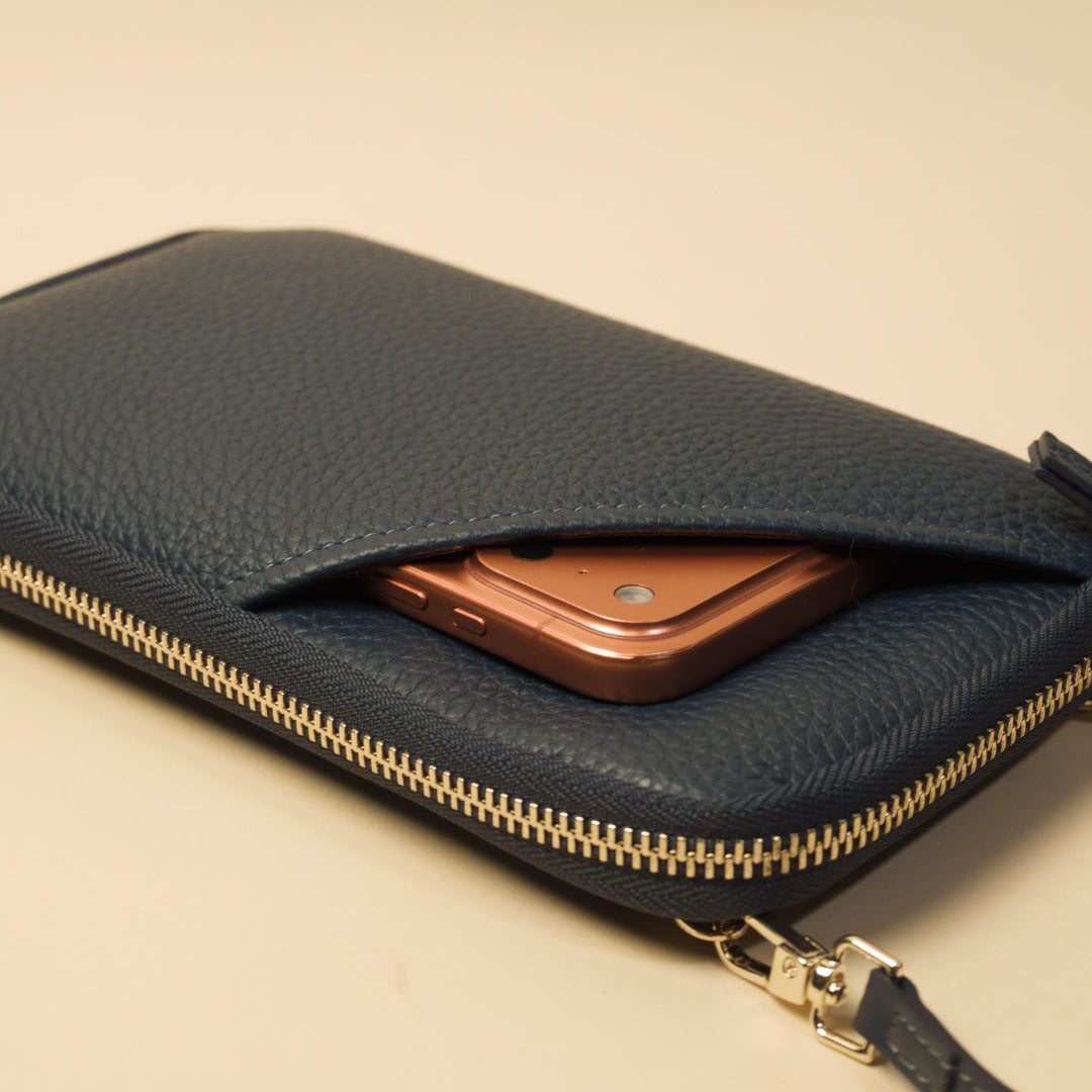 Navy blue leather wallet with gold zipper containing a copper-colored phone on a beige background