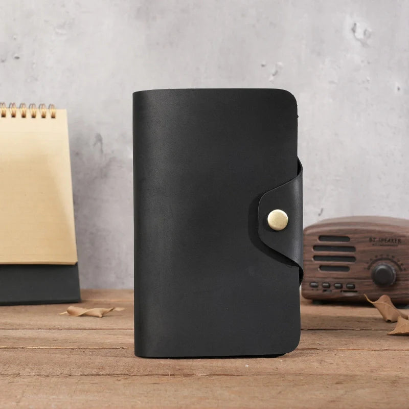 Black leather notebook with a gold buckle on a wooden surface with a concrete wall background